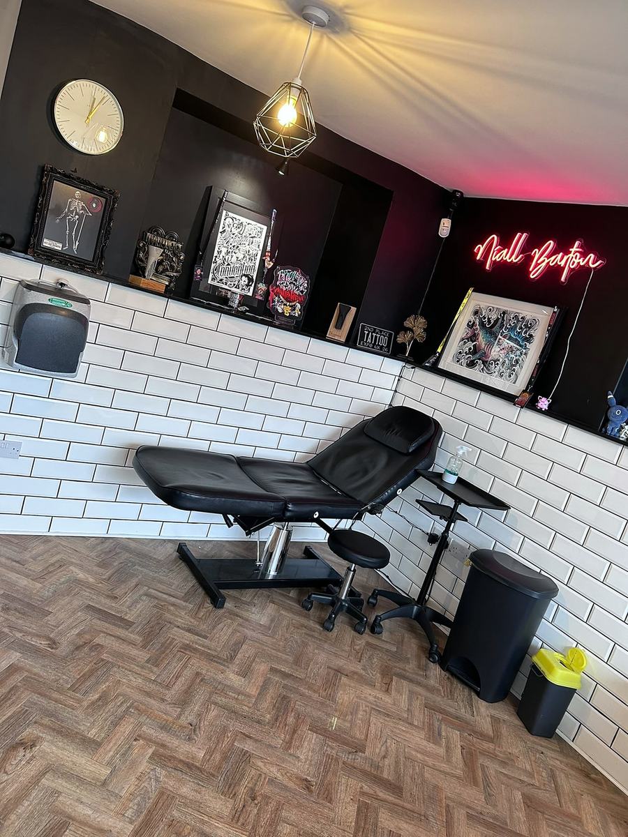 A tattoo room with a black chair, white tiles and framed art